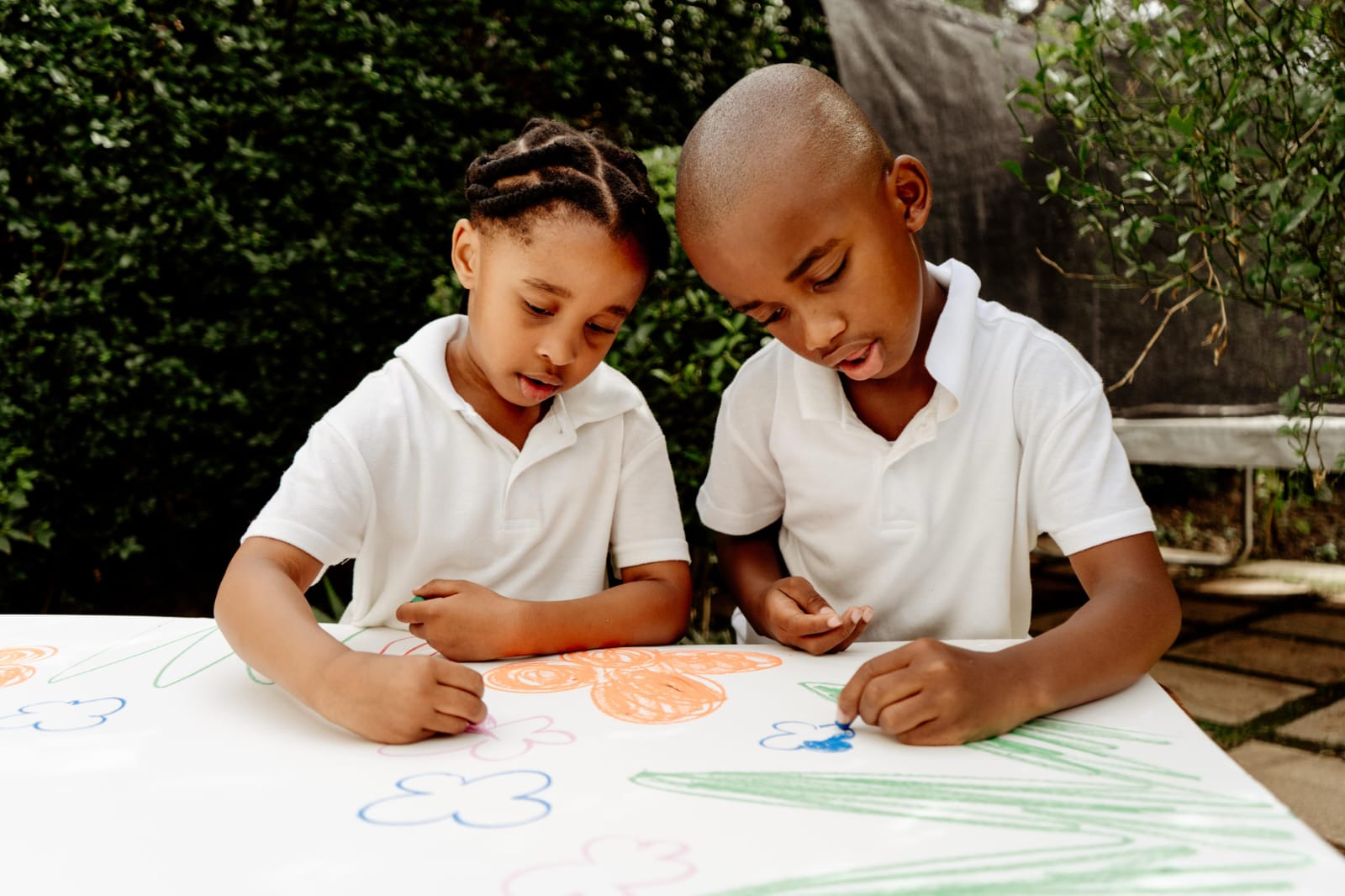 Two learners drawing flowers on a large sheet of paper at a table in the school garden