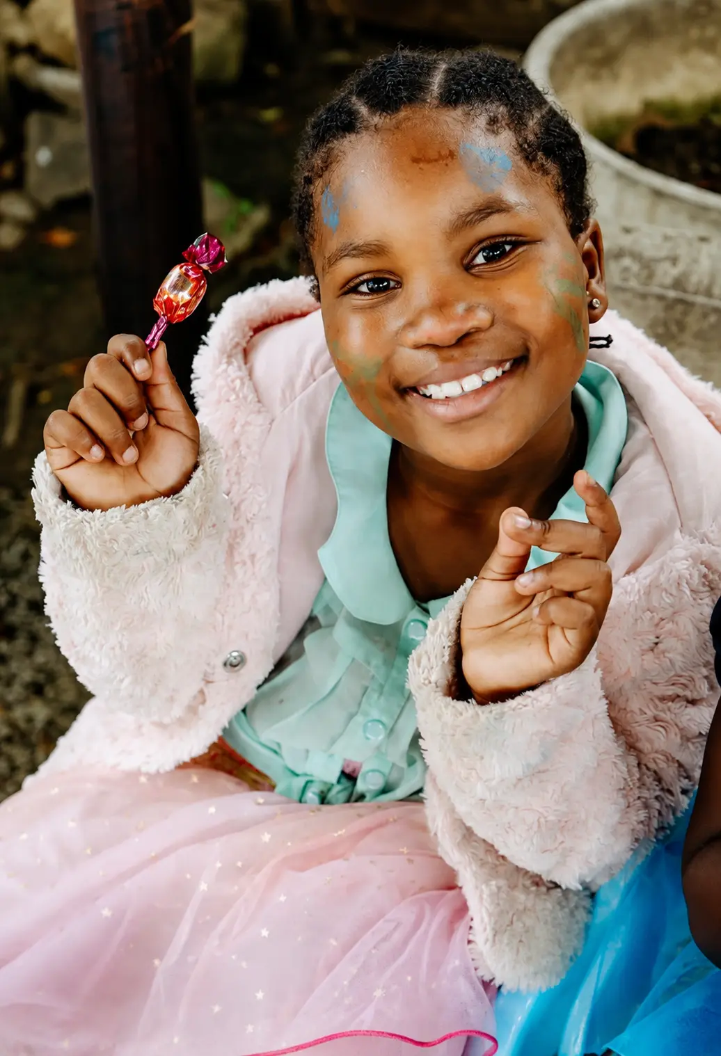A JENS learner with face paint smiling as she holds up a wrapped sweet on a dress-up day