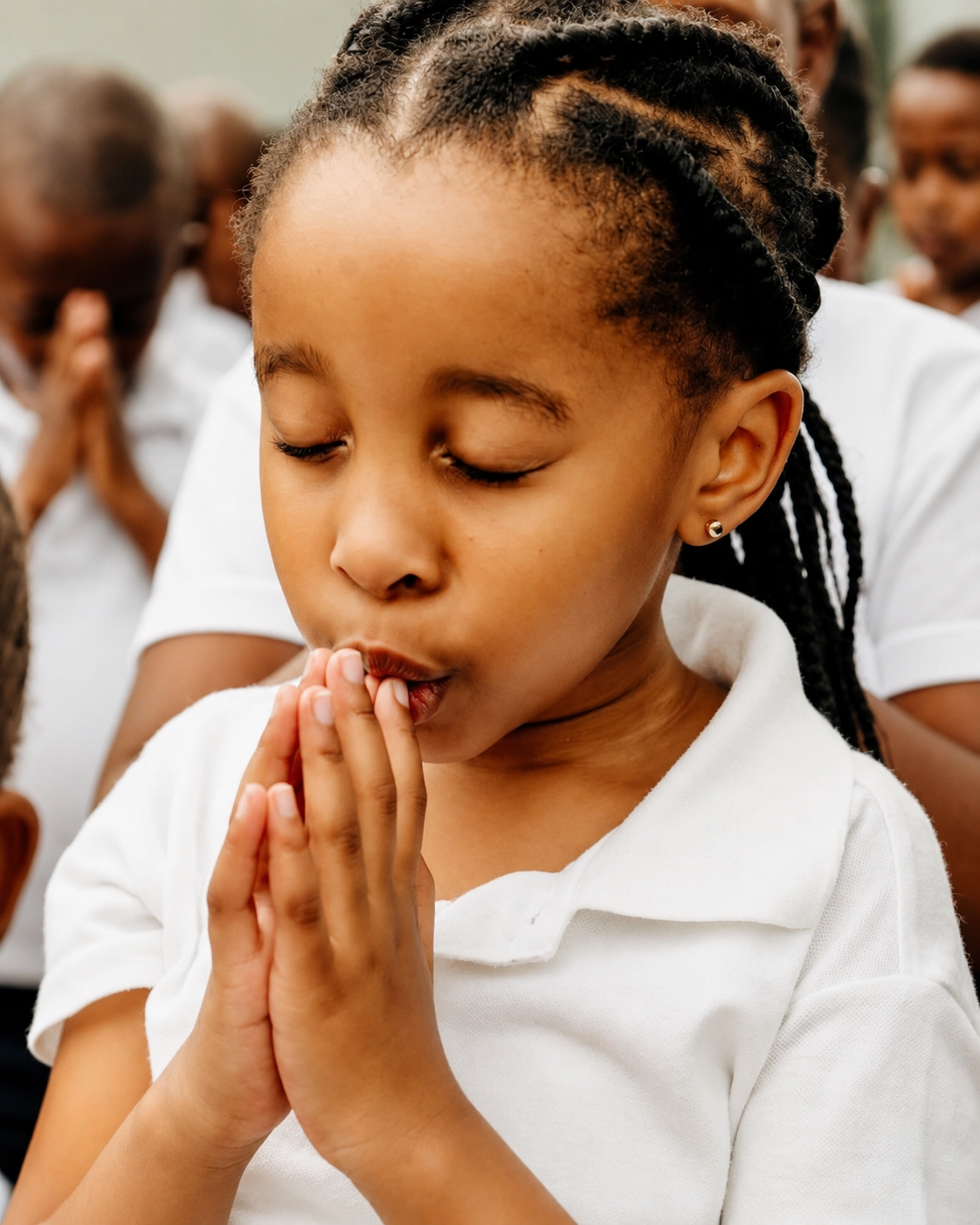 A learner in a white school shirt praying quietly with her classmates