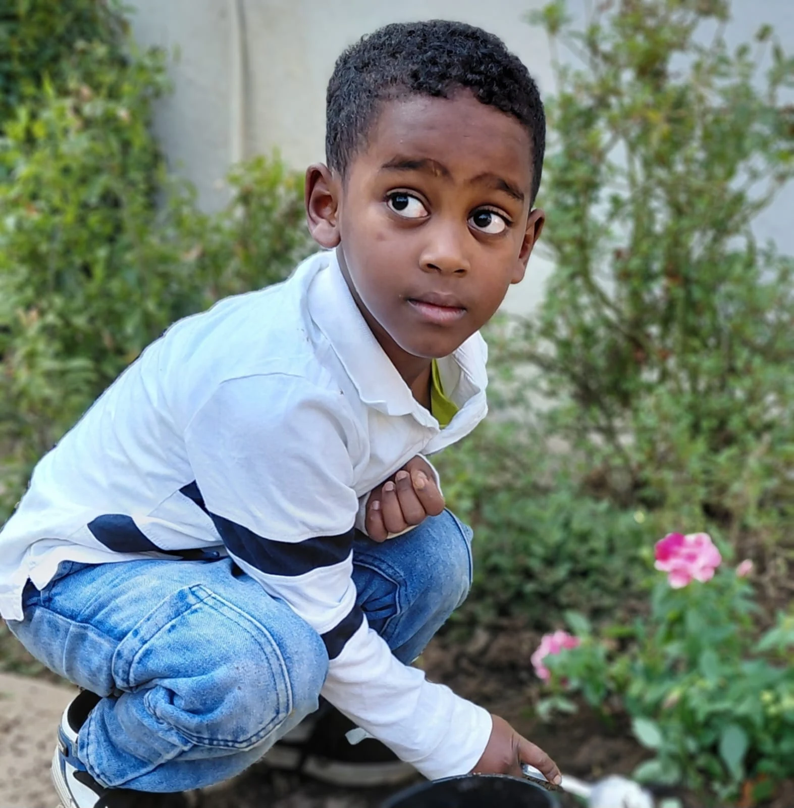 A JENS learner crouching beside the rose bushes with a planting pot on Spring Gardening Day