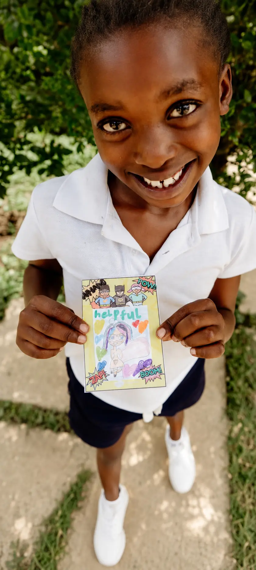 A smiling JENS learner holding up a hand-coloured card with the word “helpful” written on it