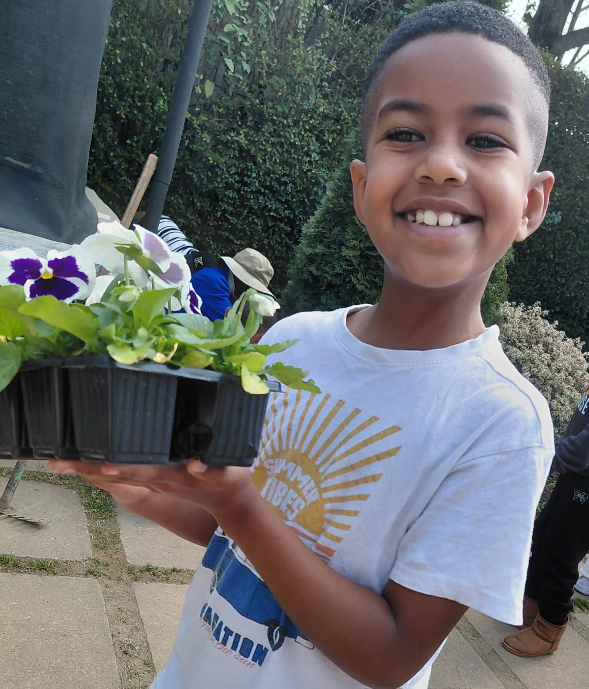 A beaming JENS learner carrying a tray of pansy seedlings donated for Spring Gardening Day