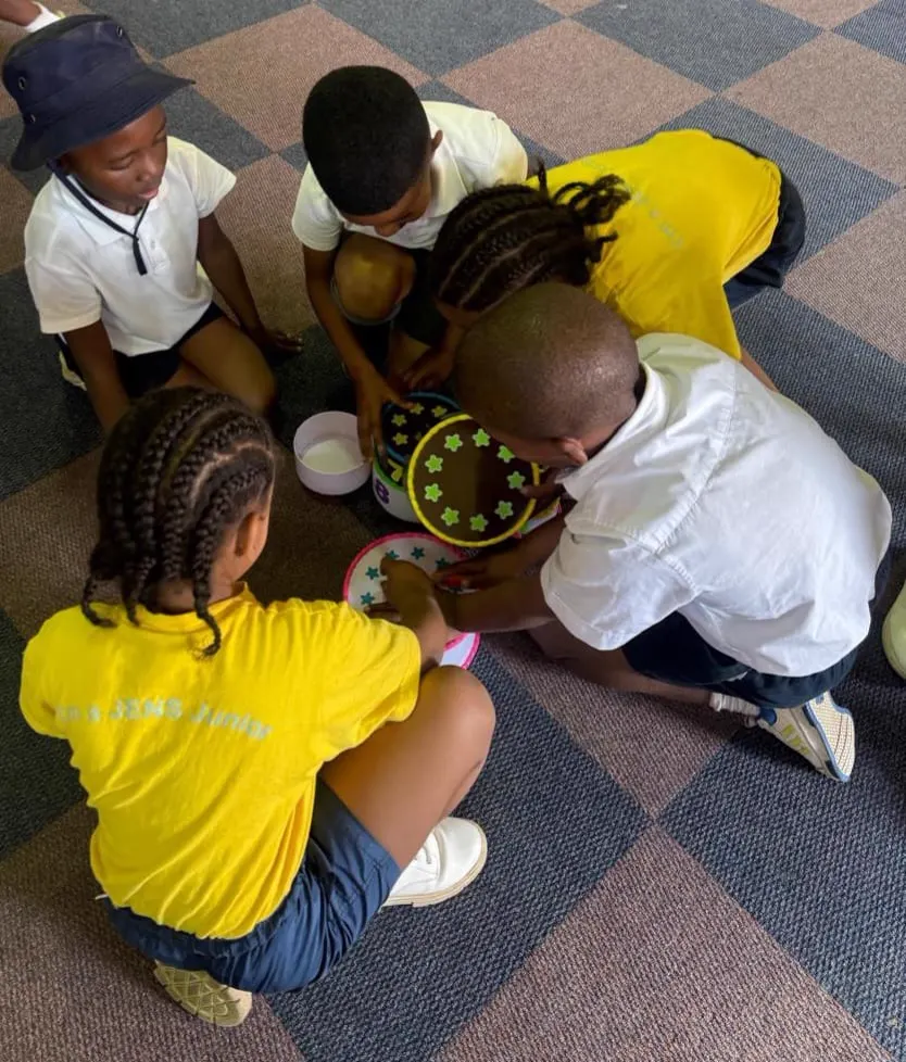 A small group of JENS learners sitting in a circle on the carpet sharing a star-patterned activity tray