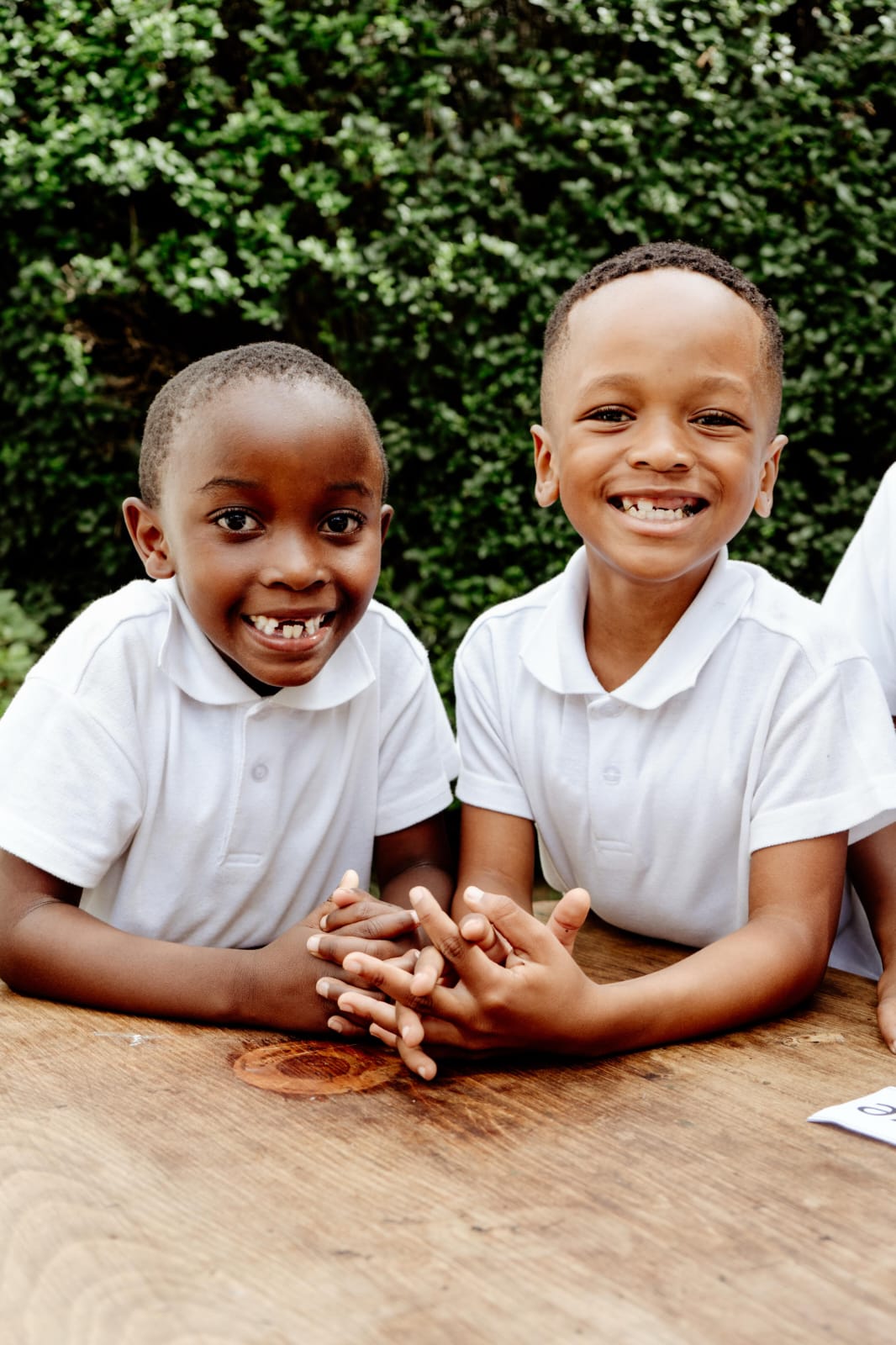 Two JENS learners in white polo shirts sitting together at a wooden table