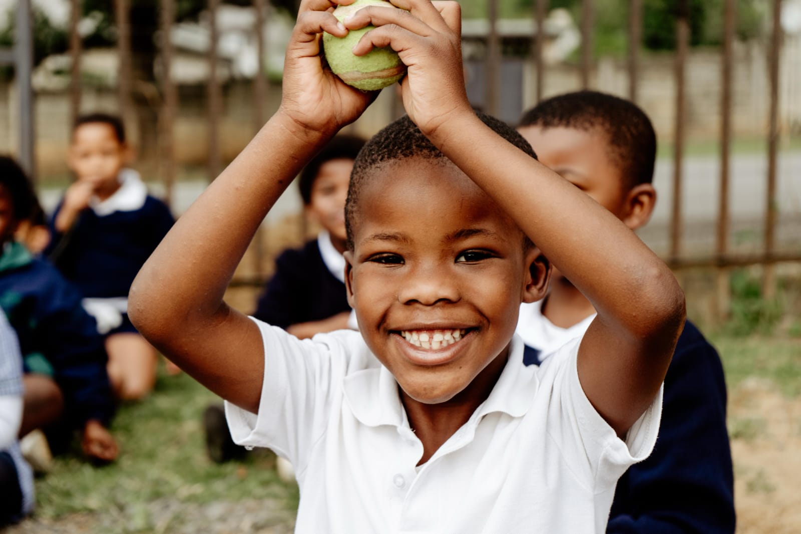 A laughing JENS learner holding a ball above his head during outdoor play