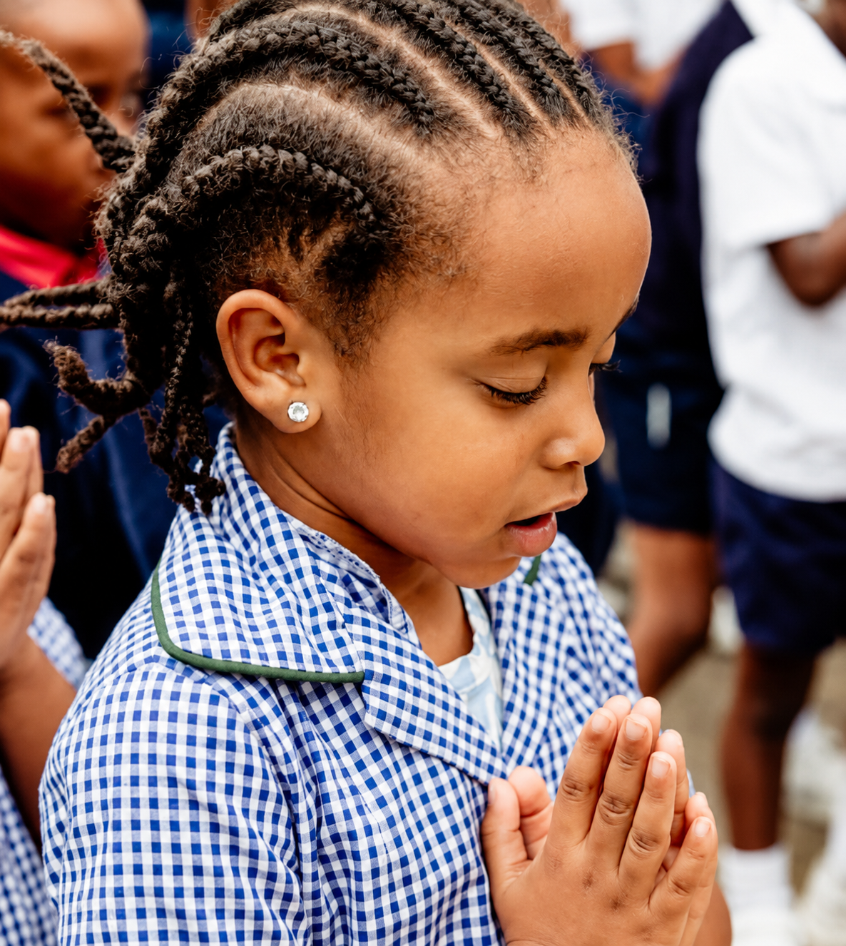 A learner in the checked blue JENS uniform with her hands together in prayer