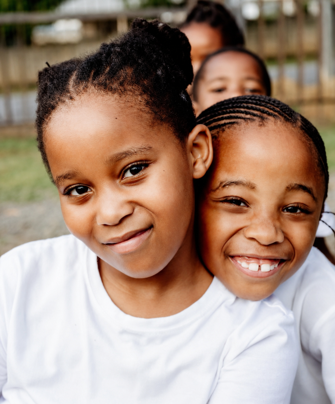 Two JENS learners in white school shirts smiling together outside