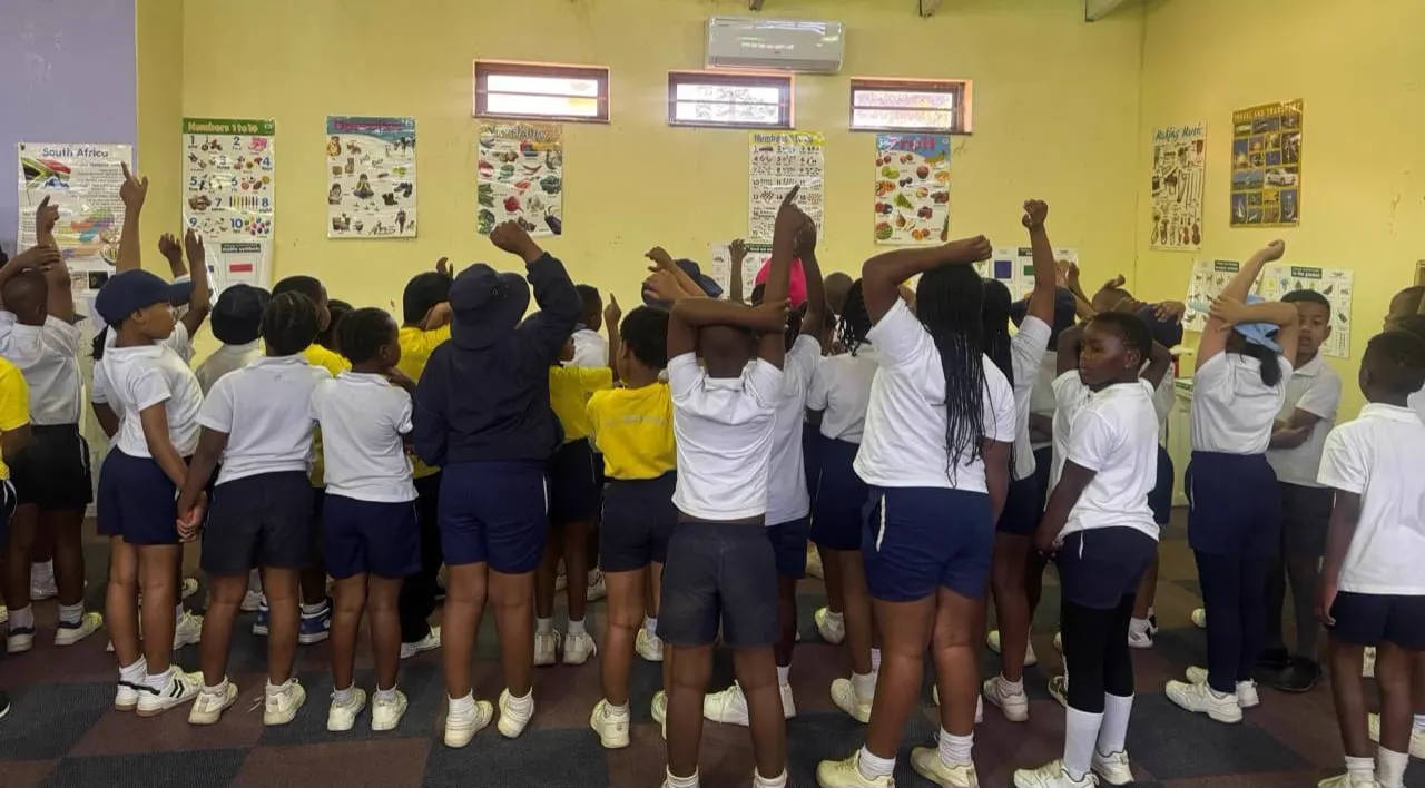 JENS Grade 1 and 2 learners standing together with arms raised during an activity at the Kokstad Library