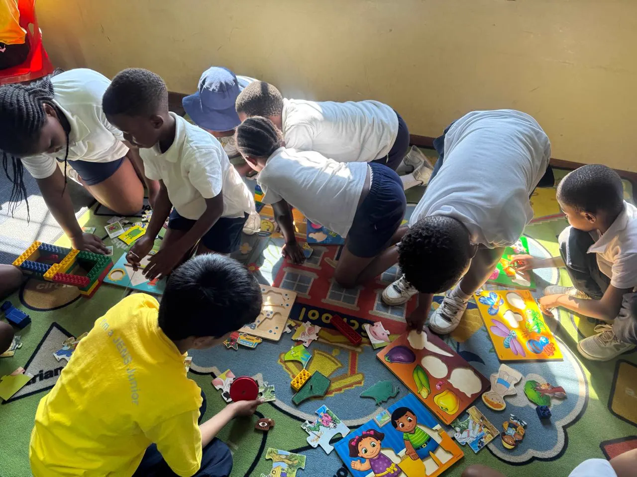 JENS learners kneeling on a colourful play mat building wooden puzzles and blocks in the library activities room