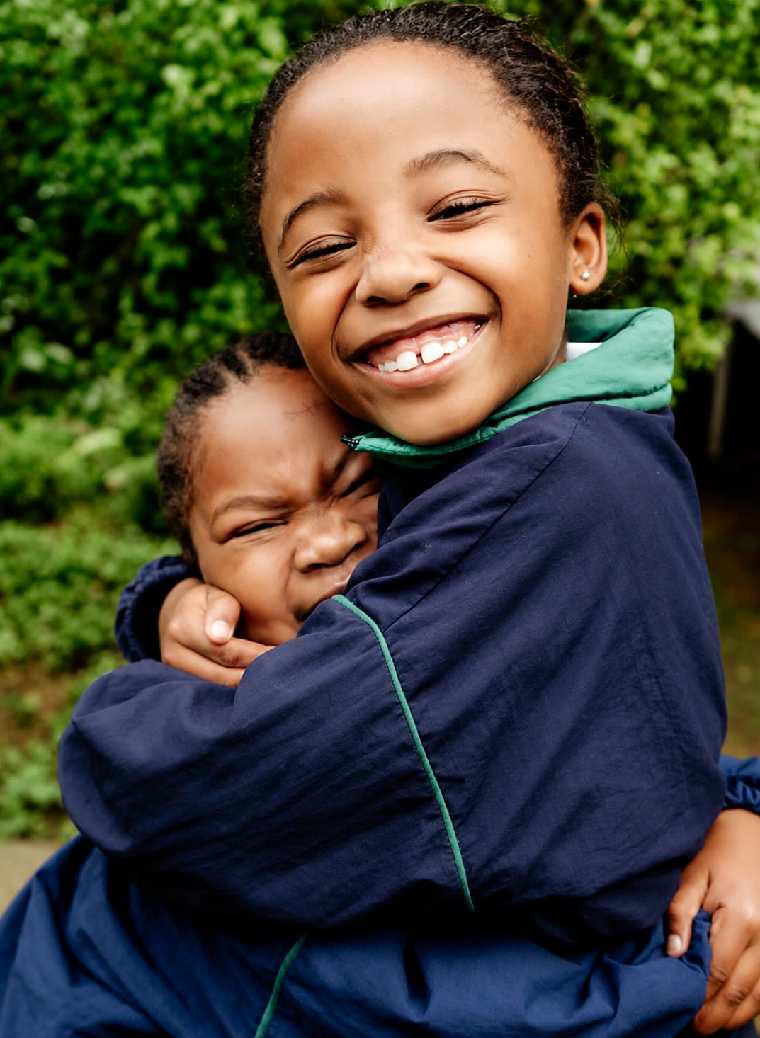 Two JENS learners in navy school jackets hugging and laughing together outside