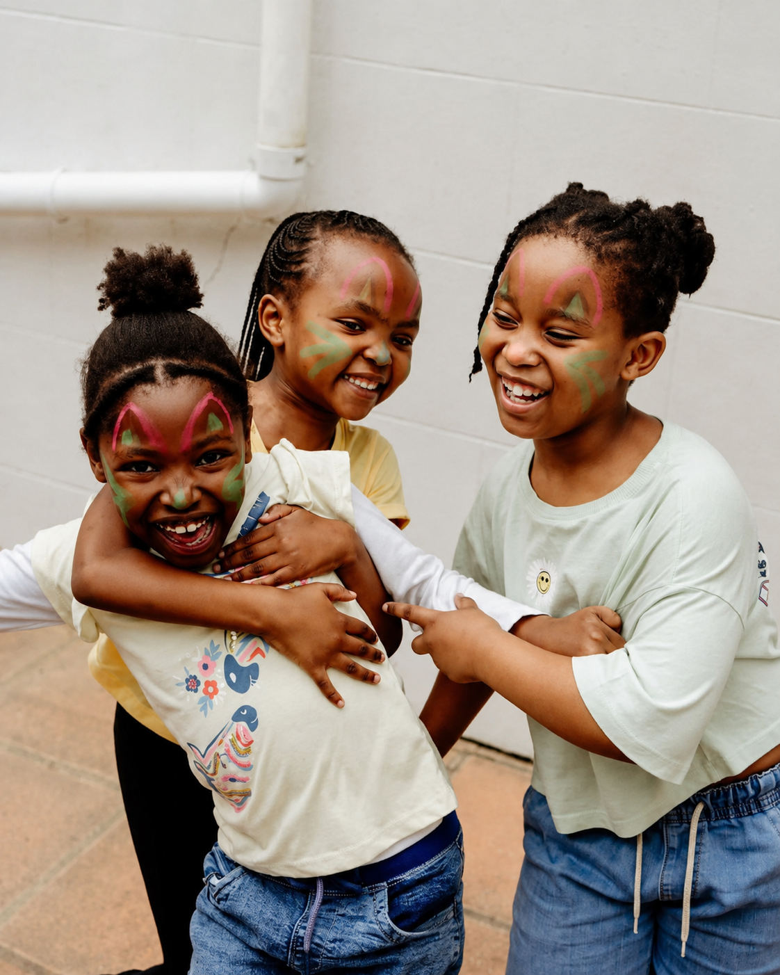 Three JENS learners with painted faces laughing and hugging each other on a special dress-up day