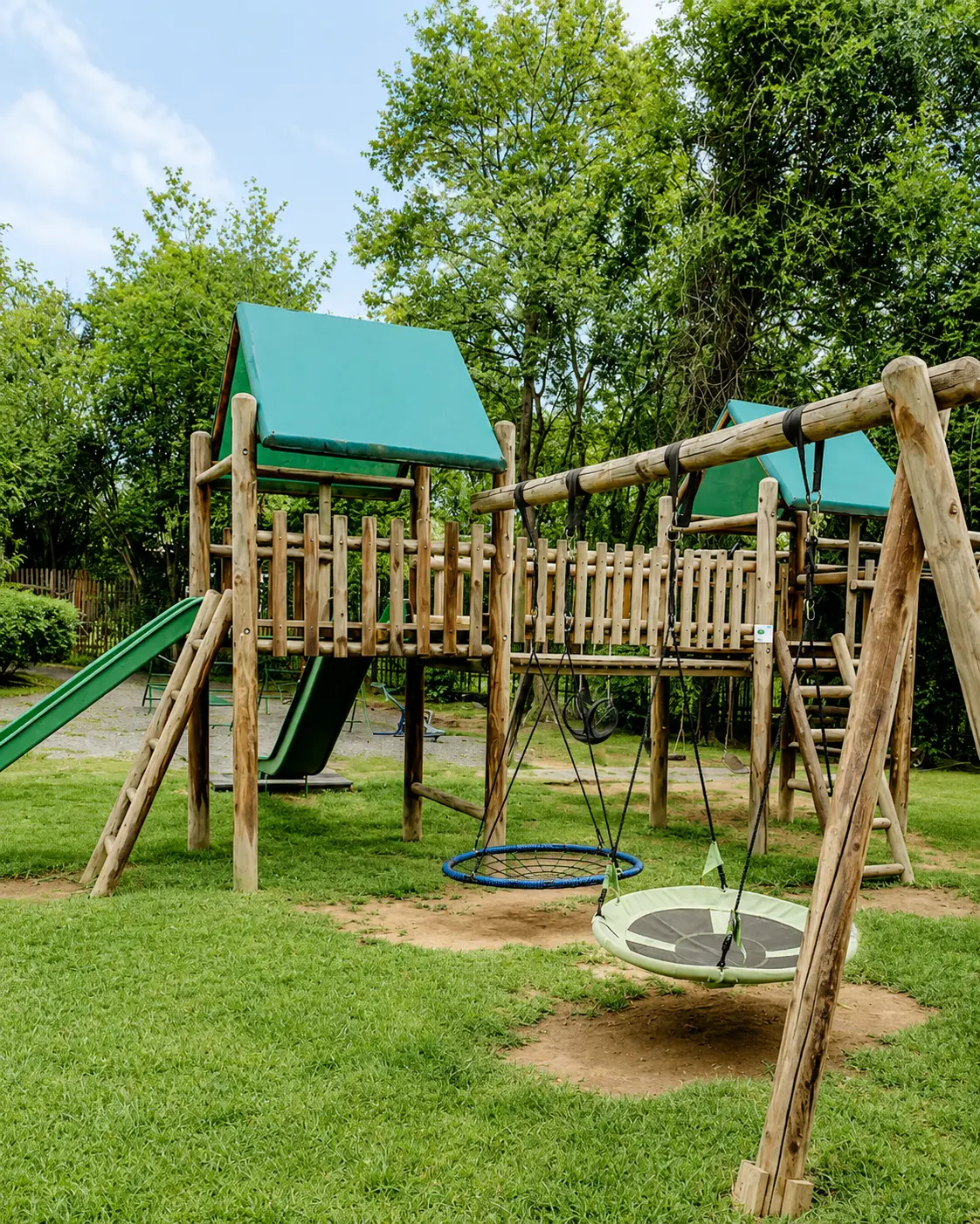 The JENS playground with a wooden climbing frame, slide and two nest swings on the grass